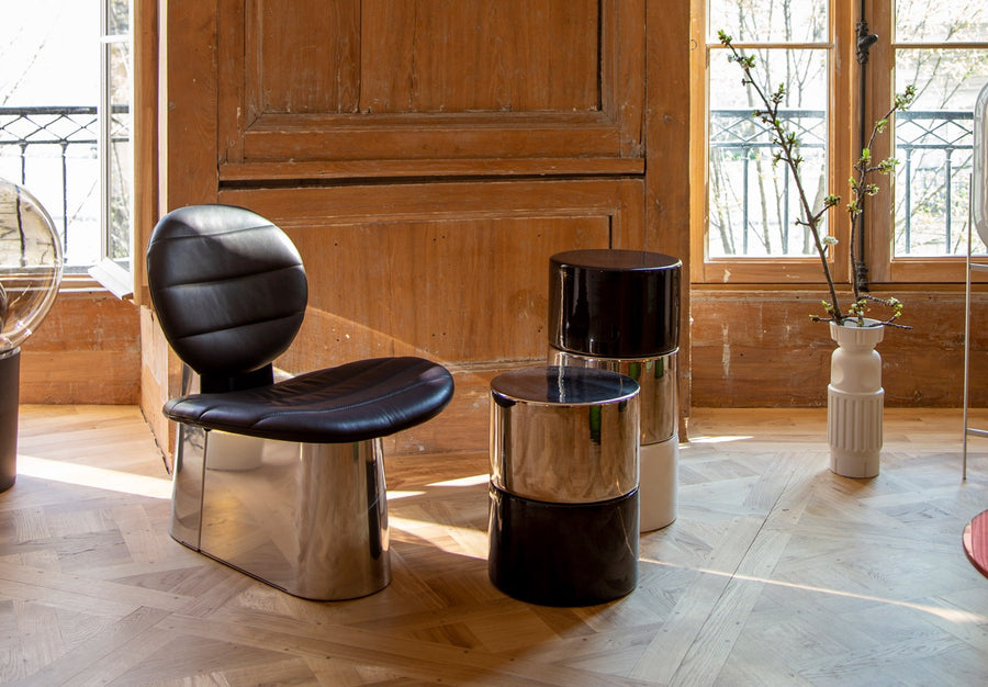 Pilota lounge chair in black leather with silver base next to side tables in a living room